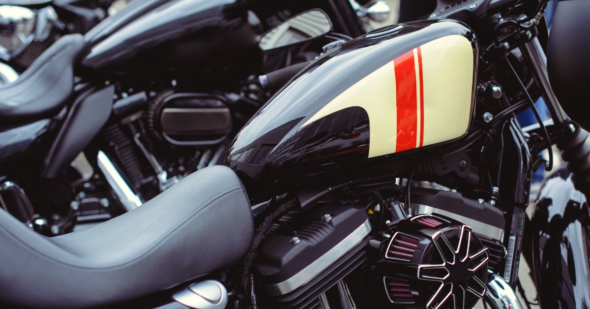 A black motorcycle gas tank with cream-and-red striped graphics, chrome details, and a glossy curved surface.