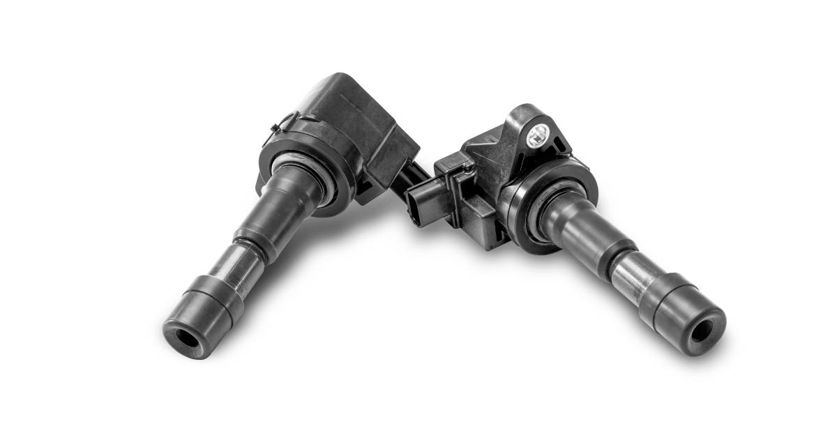 Two black ignition coils for gasoline engines next to one another isolated against a white background.