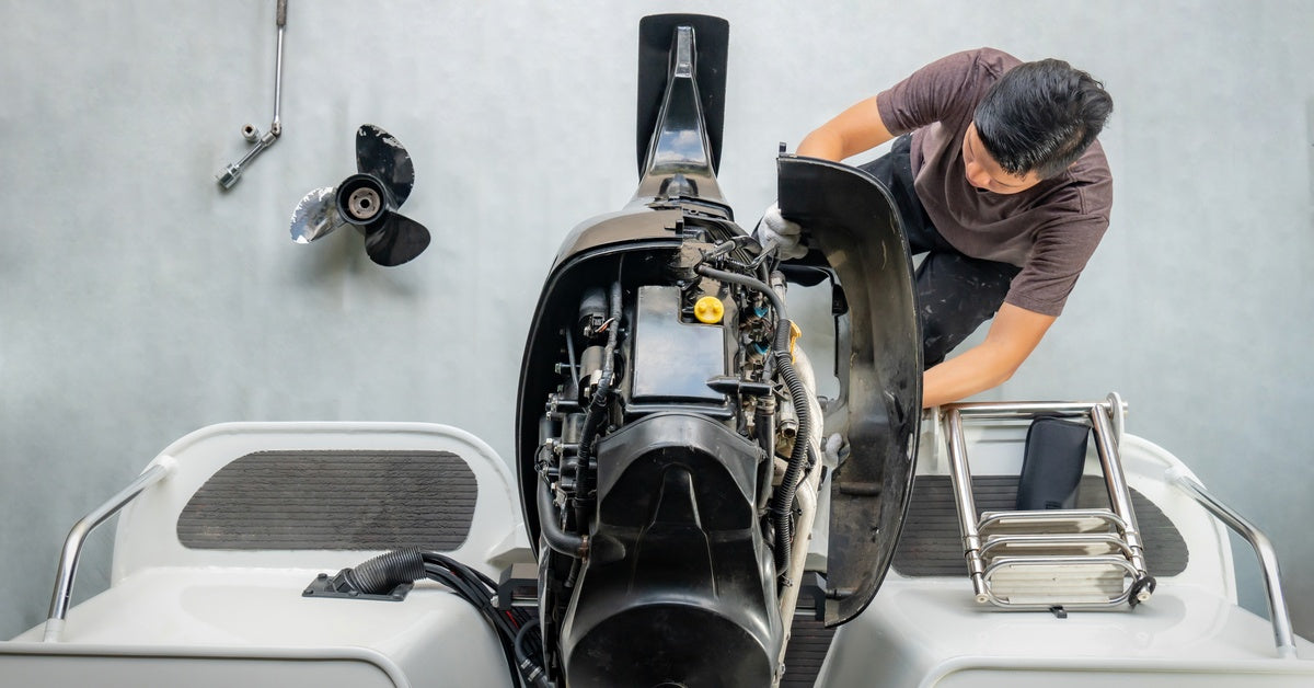 A technician disassembles a boat's engine for maintenance and repair. A single propeller lies on the floor.