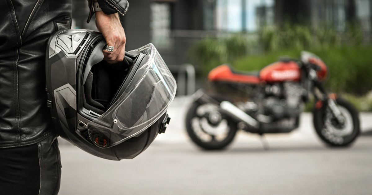 A motorcycle driver holds a safety helmet in their hand as they approach their parked bike in the distance.