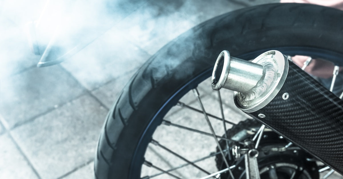A close-up of a cloud of white smoke coming out of a motorcycle's black exhaust pipe and spreading in the air.