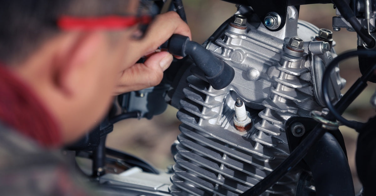 A mechanic disconnects the hose covering the spark plug of a motorcycle and inspects its condition up close.