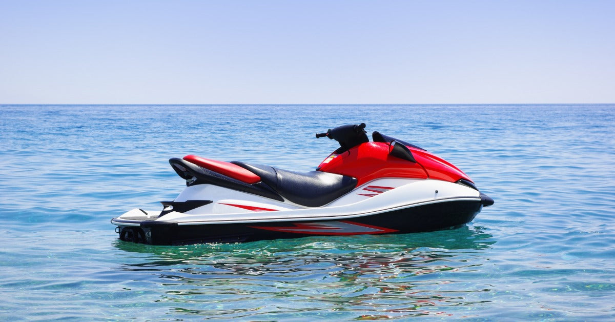 A shiny jet ski with red accents and white detailing floats on open water beneath a bright, cloudless sky.