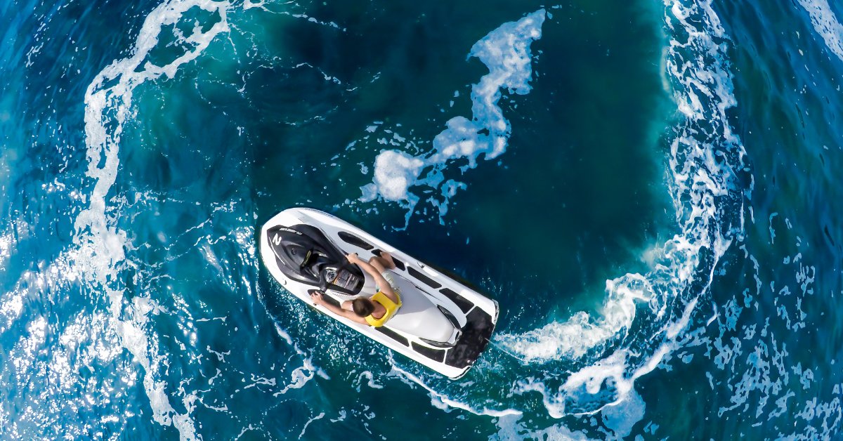 A top view of a person riding a personal watercraft across blue ocean water, leaving white spray behind the vehicle.