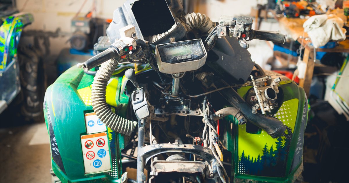 A close-up of a disassembled ATV engine in a garage, with parts and metal components arranged closely together.