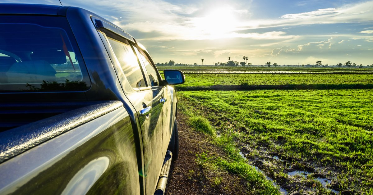 A black truck parked on a green field points in the direction of a setting sun. There are clouds in the sky.