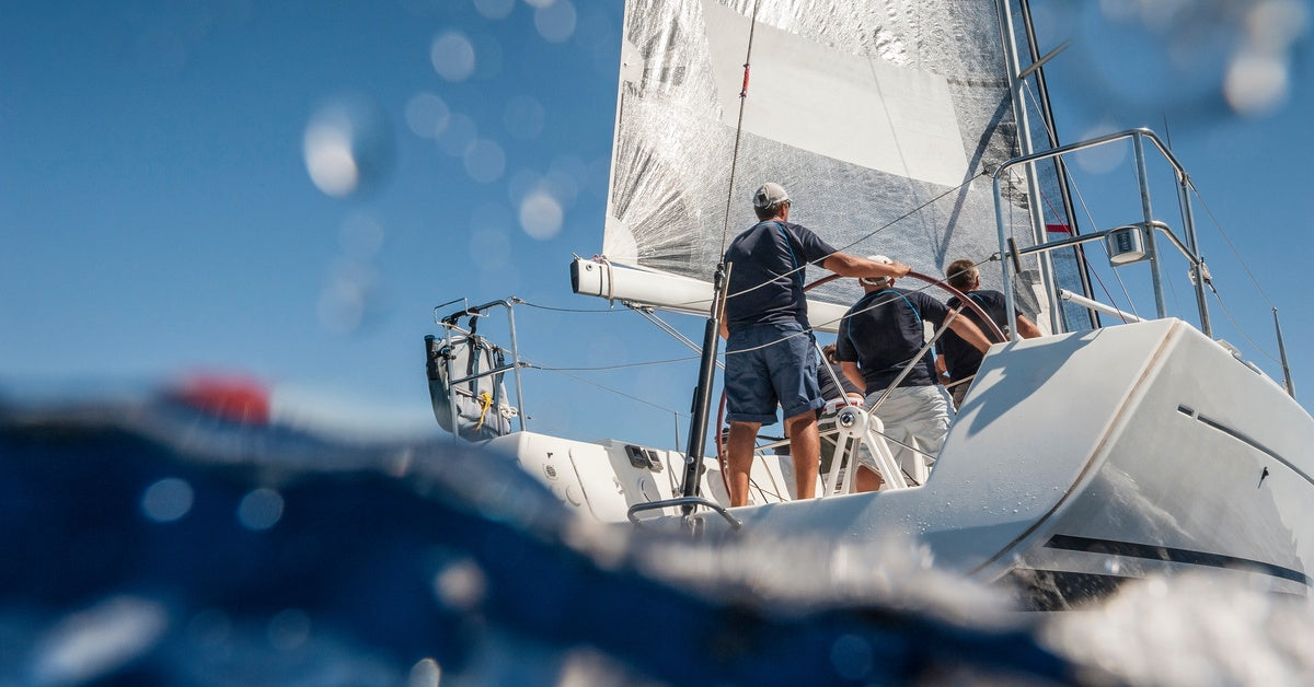 A low-angle view of a sailboat partially obscured by water, with four people on board wearing matching shirts.
