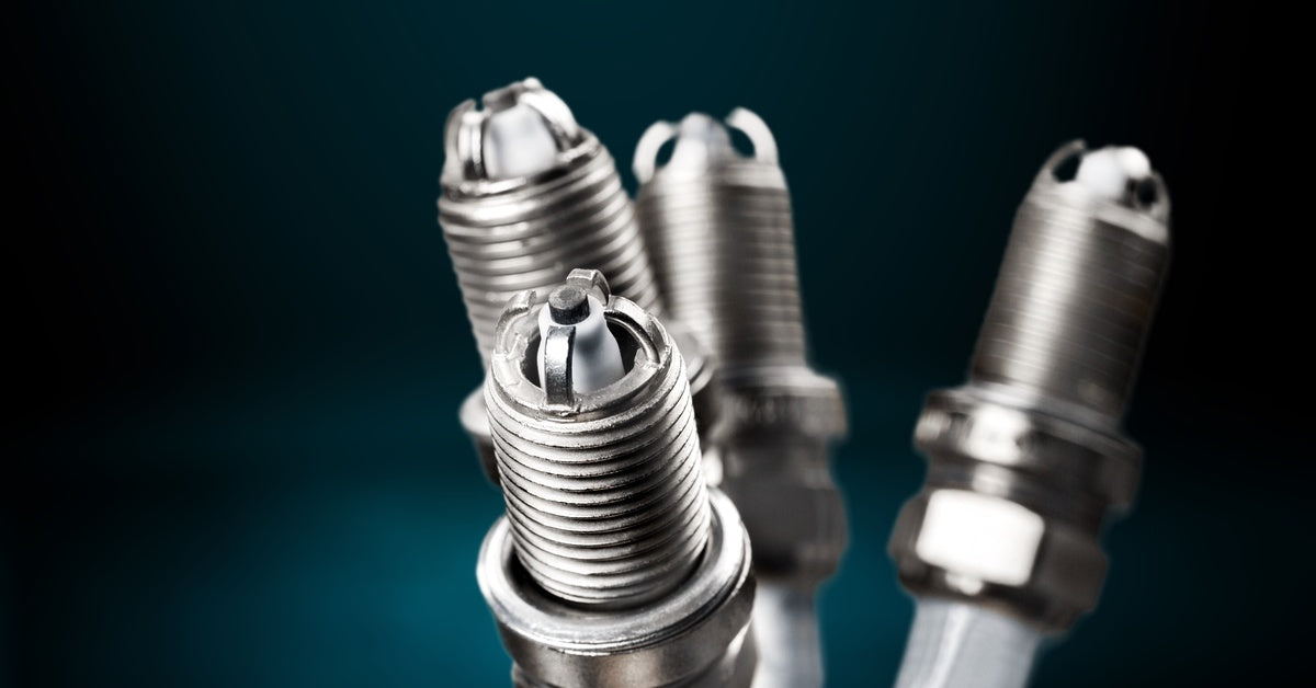 Four spark plugs with multiple ground electrode tips are displayed against a blue gradient background.