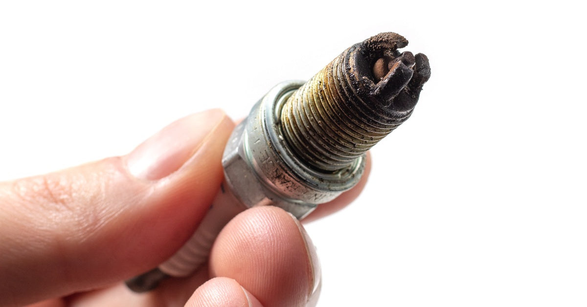 An extreme close-up of a person holding a spark plug with a dirty electrode tip against a white background.