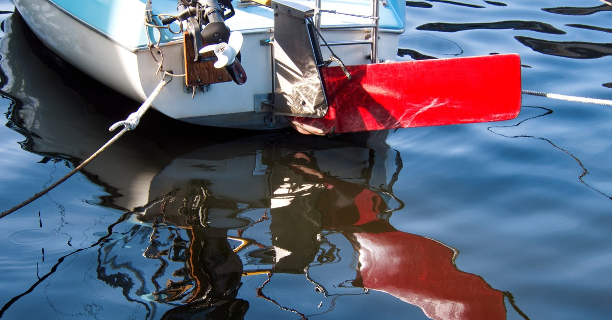 A small boat's stern with an outboard motor floats on rippled dark blue water, alongside a bright red buoy-like object.