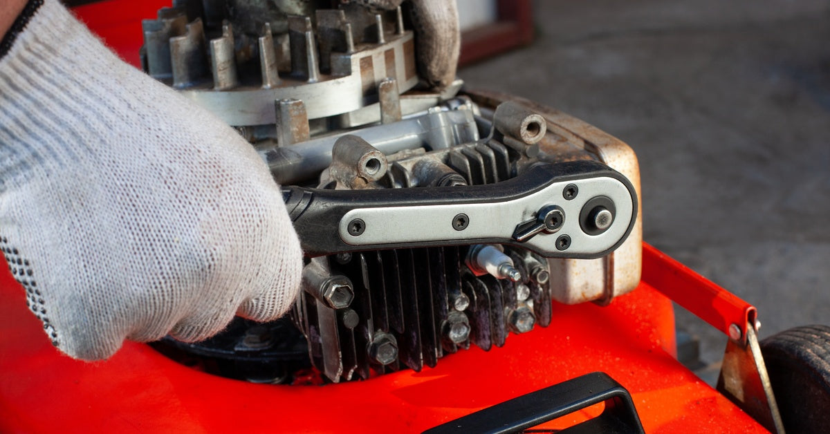 A close-up of a person wearing white gloves and using a ratchet wrench on the engine of a red lawn mower.