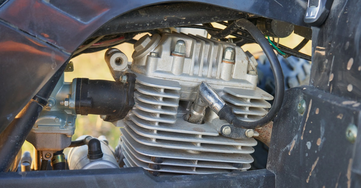 An ATV engine and cylinder head with cooling fins, spark plug wire attached, and surrounding frame components visible.