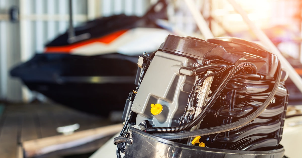 A close-up view of a small marine engine with visible tubes. A jet ski is seen in the background of the garage.