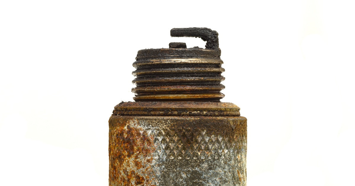 A heavily corroded spark plug with rust, grime, and carbon buildup is centered against a plain white background.