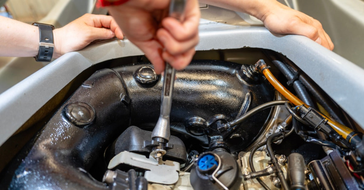 A person uses a socket wrench to remove a spark plug inside a jet ski engine compartment during maintenance.