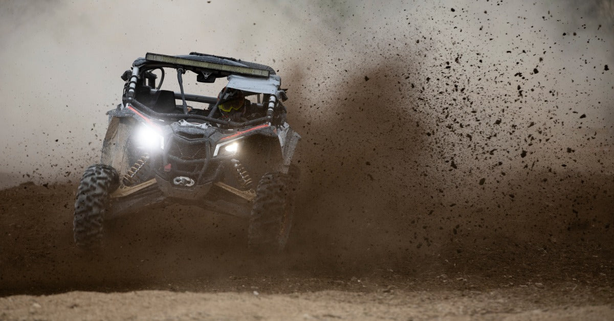 An off-road vehicle drives through mud, splashing dirt as it navigates rough terrain during an outdoor adventure.